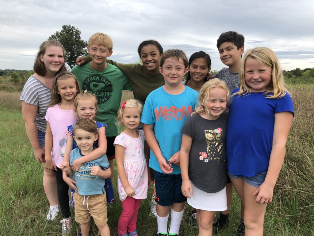 A group of kids standing together in a field with the FHPS tree behind them