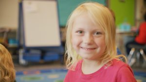 A kindergarten girl with blonde hair smiling