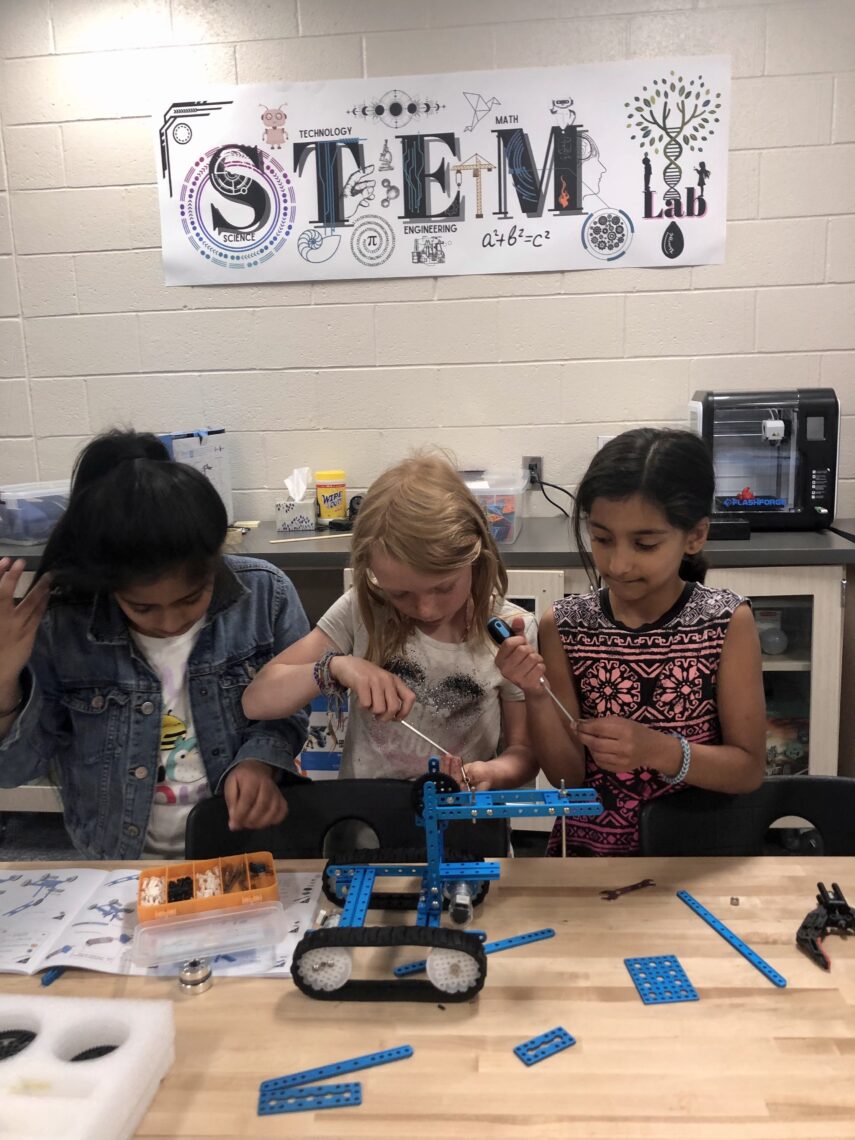 Three elementary students building a robot.