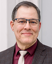 middle age man in a brown suit and burgundy shirt and white tie