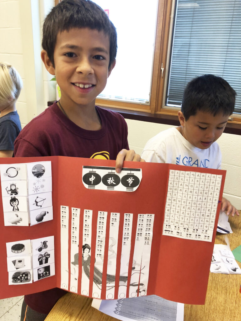 An elementary school boy holds up a learning tool he is creating in Chinese