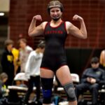 A female high school wrestler flexing her muscles and smiling.