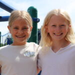 Two girls standing next to each other on the playground.