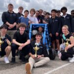 students gather around an electric vehicle with trophies