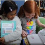 screen shot from YouTube video of two girls reading in a school media center