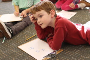 a little boy lays on his stomach to draw an image