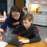a teacher looks at a computer with a student