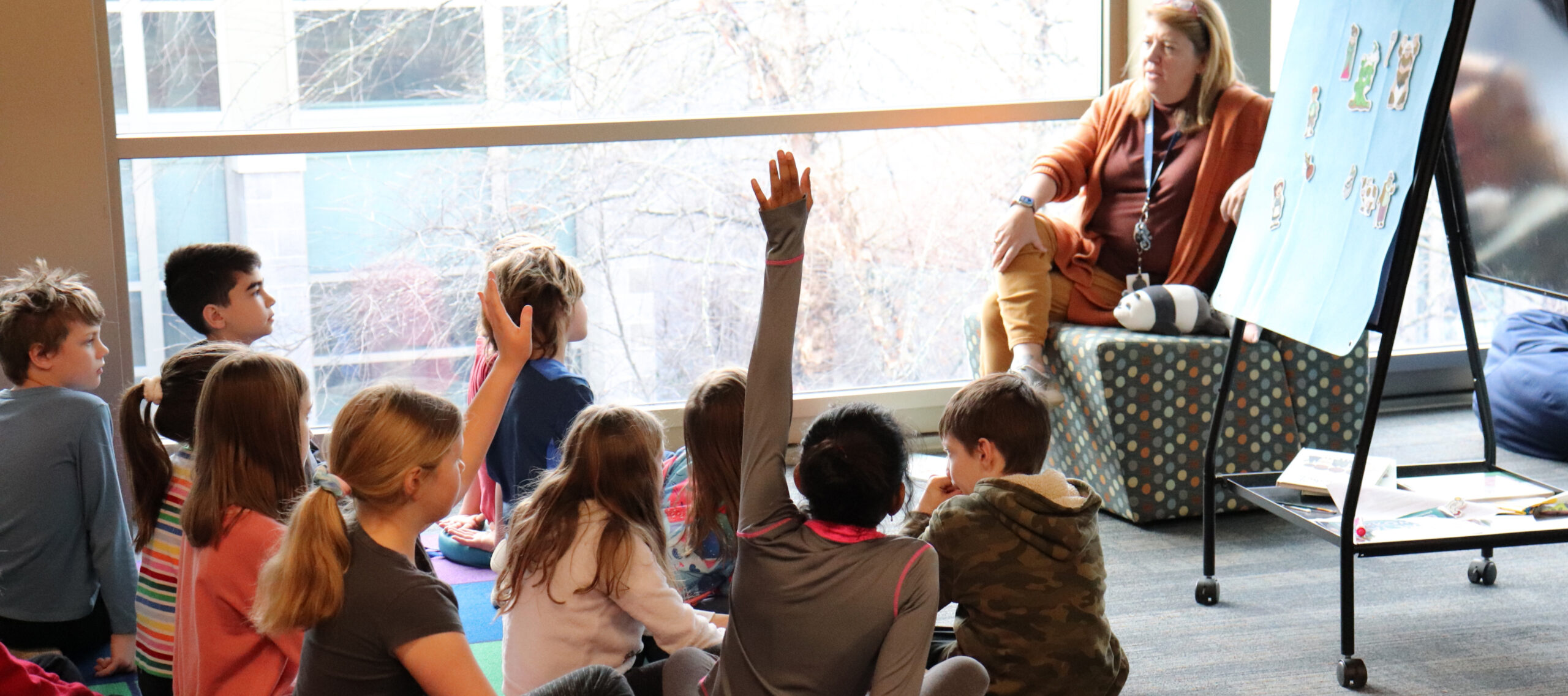 students in class sitting on floor with some raising their hands