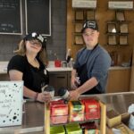 two older students holding cups of coffee behind a counter