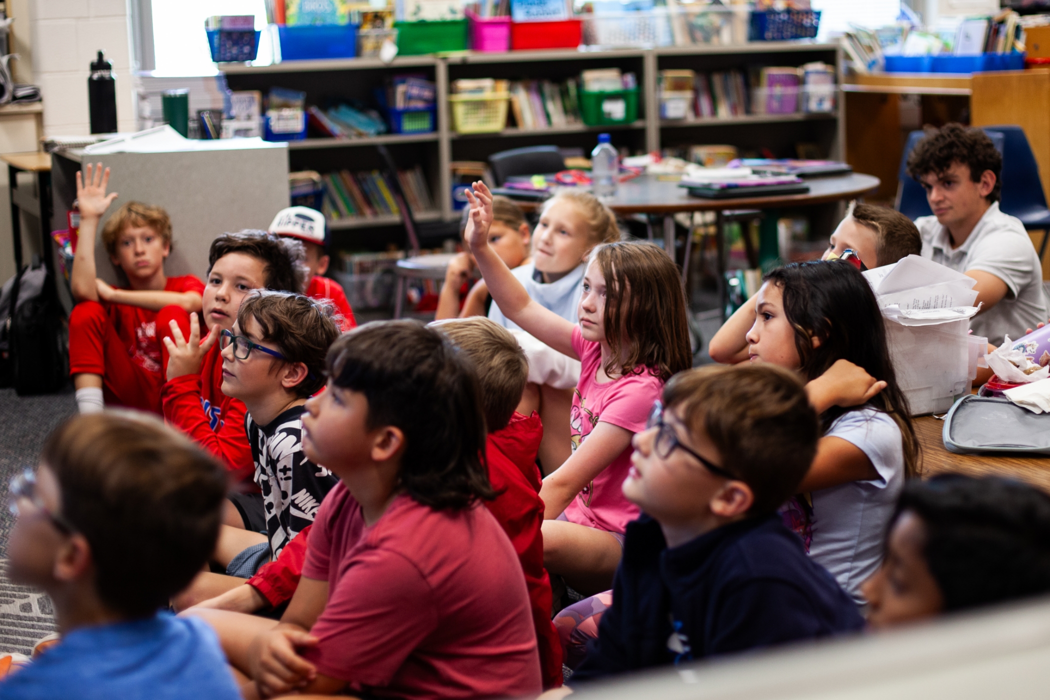 students in class sitting on floor with multiple hands raised