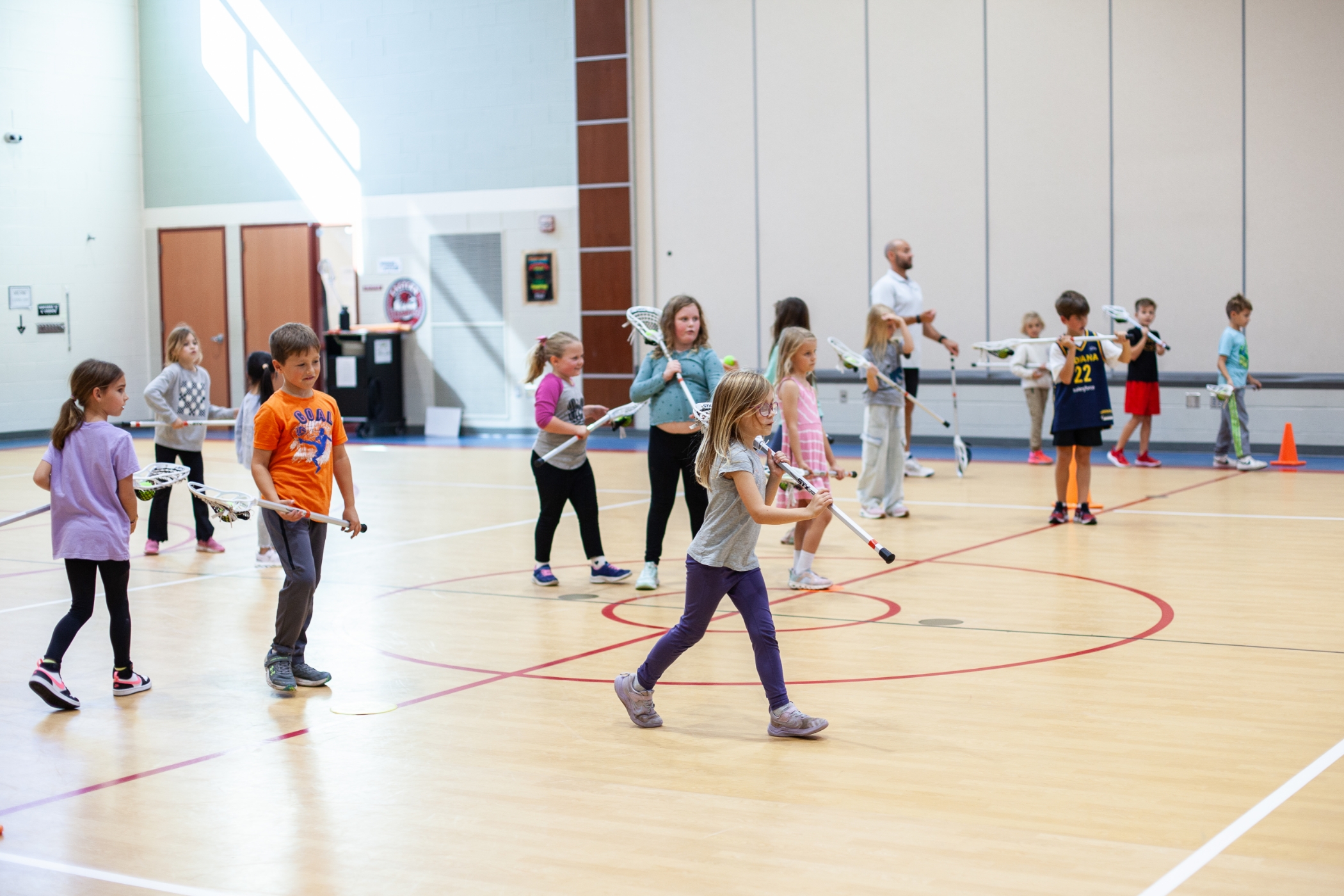 young students playing lacrosse in a gym