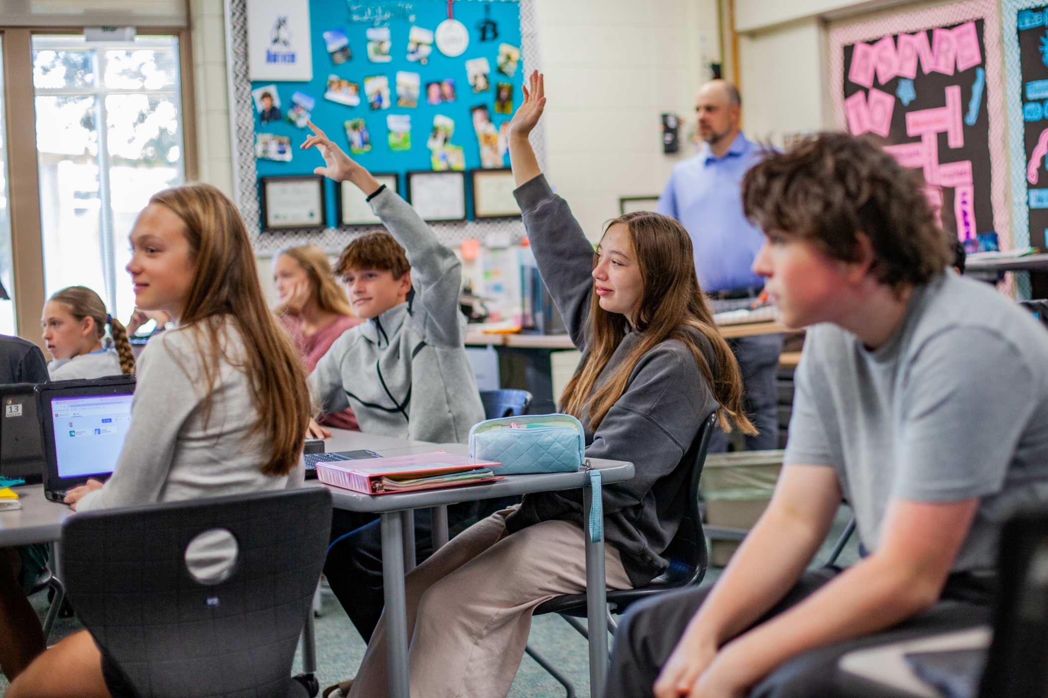 students in a classroom with two students raising their hands