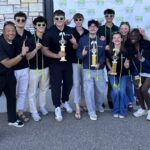 a group of high school students hold up the number 1 sign while holding on to three trophies