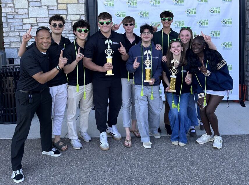 a group of high school students hold up the number 1 sign while holding on to three trophies