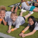 three fourth grade girls lay on a football field smiling and having fun