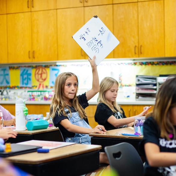 two young girl students holding a whiteboard with asian language text written on it