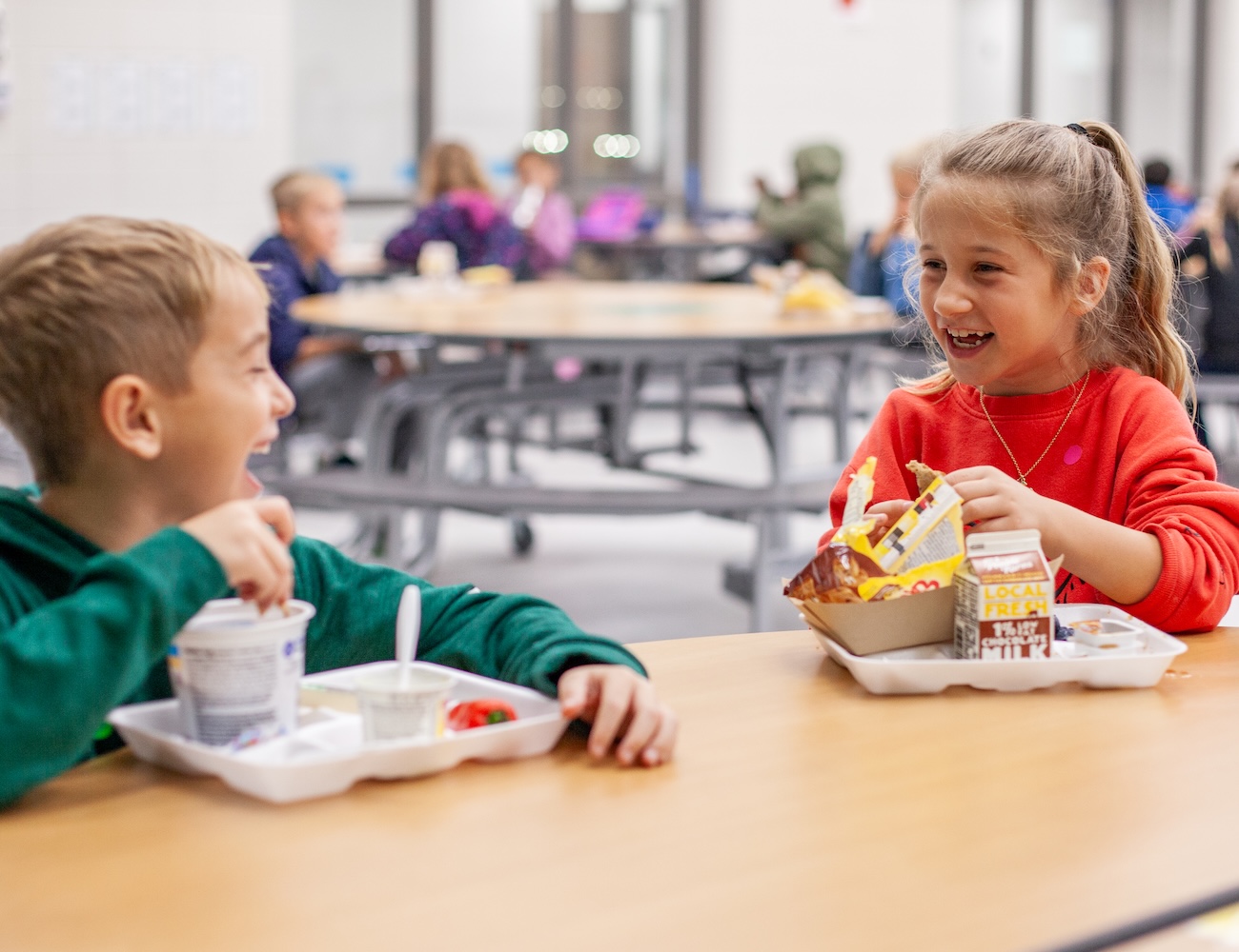two young kids eating lunch together laughing