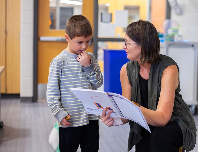 teacher showing young elementary student something in a book