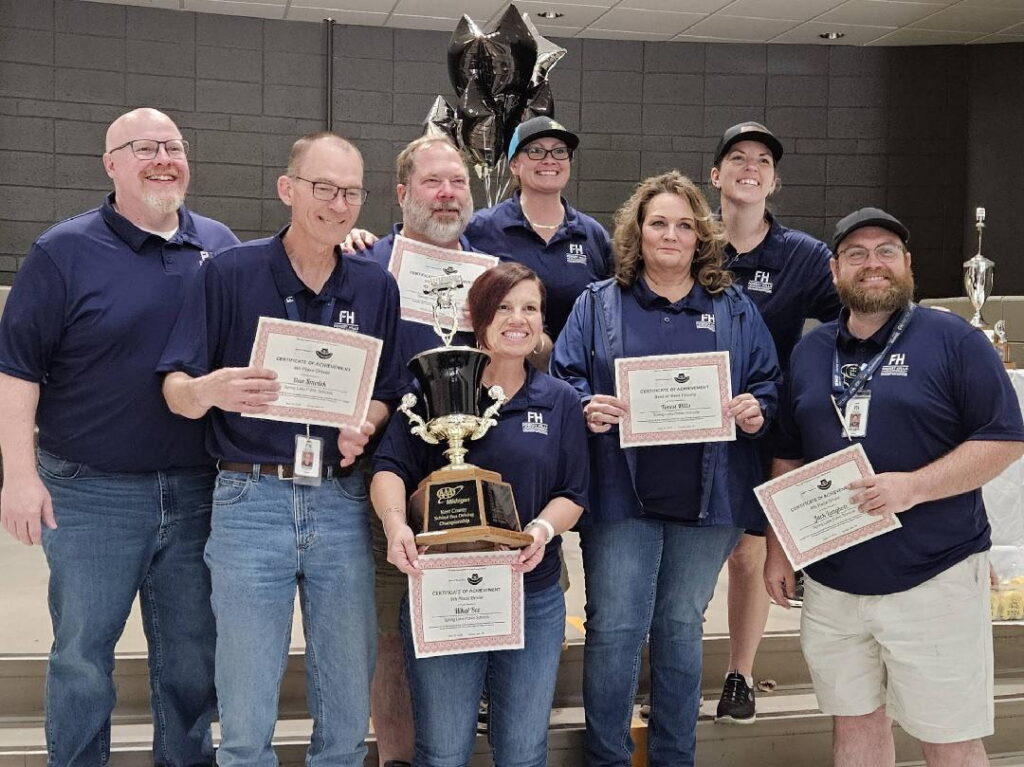 eight adults gather and hold up a trophy and certificates
