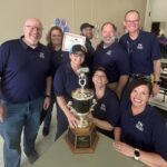 eight adults hold up a trophy