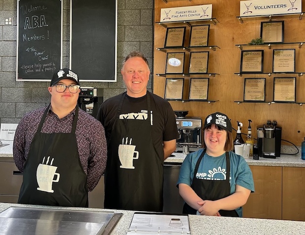 staff member and two students smiling for a picture as they work behind the desk at a coffee shop