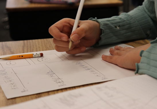 student writing on paper in Mandarin in immersion class
