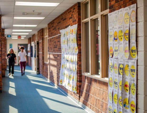 students walking down a hallway lined with different emojis drawn by students