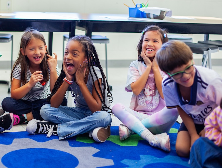 young elementary students laughing and sitting on the floor