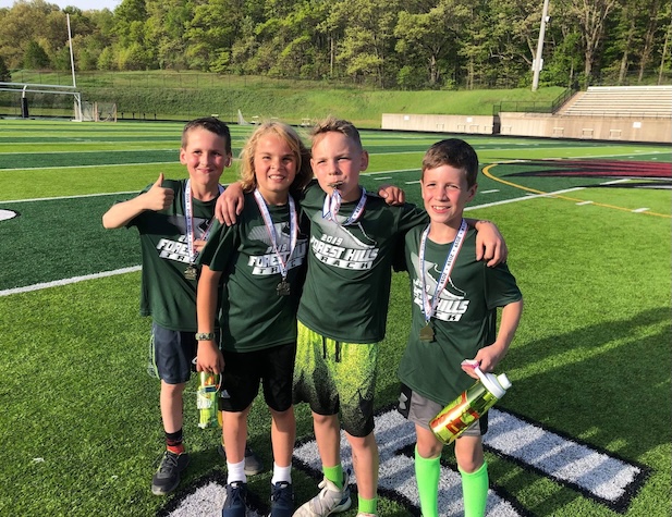 four young students on a field showing their medals from a track event