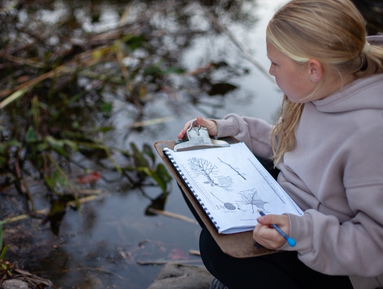 student in a creek with a clipboard