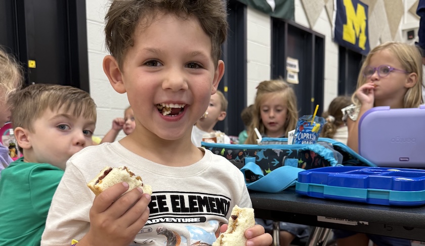 young male student eating a sandwich and smiling at the carmera