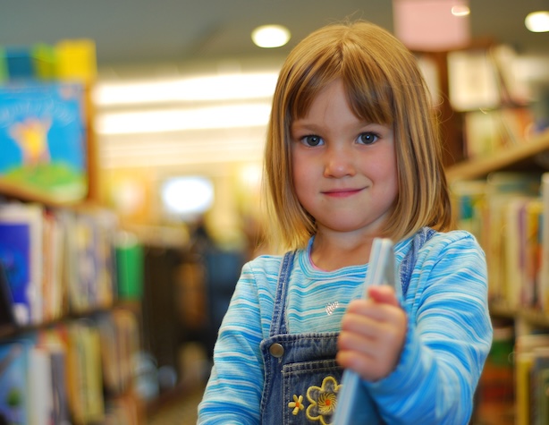 young female student in a library holding her book and smiling