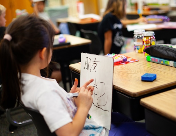 young student in class writing in a foreign language on a whiteboard