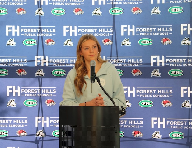 female student giving a speech at a podium in front of a forest hills backdrop