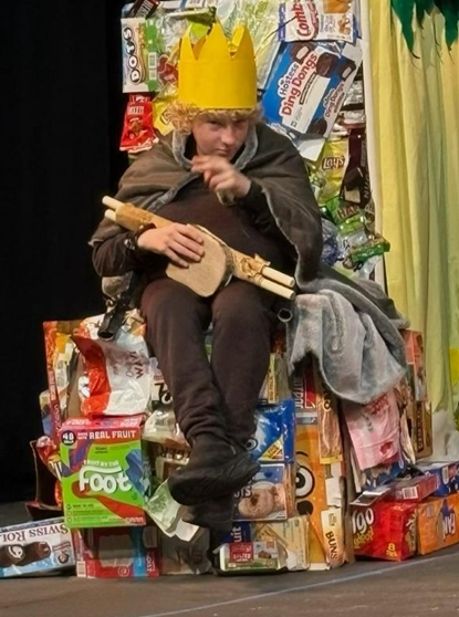 a student acts as a king and sits on a throne made of garbage