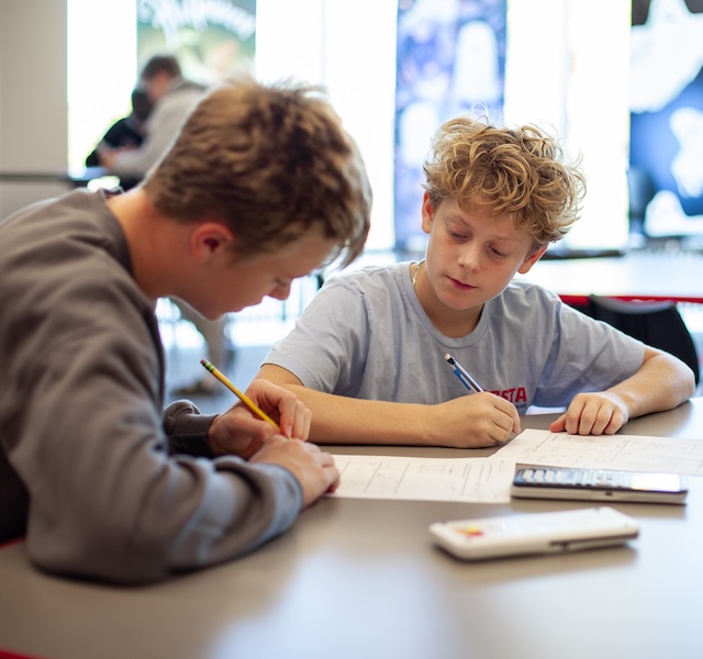 two male students working on a writing on a paper at their desk
