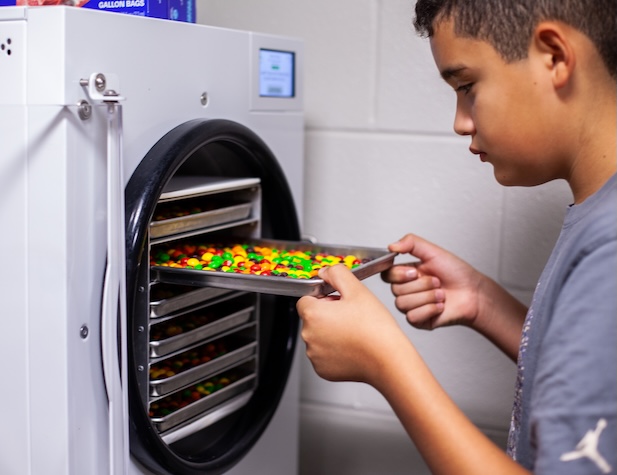 male student putting Skittles in an oven as a project