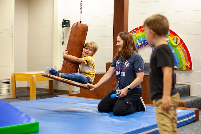student balances on a swing with the help of a teacher