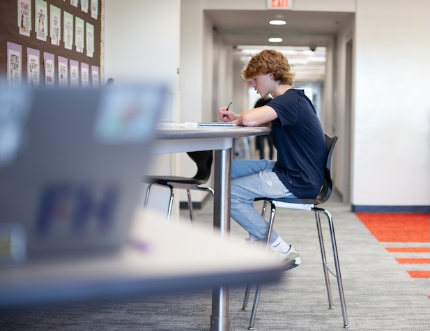 male student working at a table in a hall