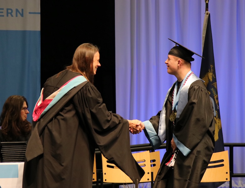 student graduating walking across the stage and shaking hands with a staff member