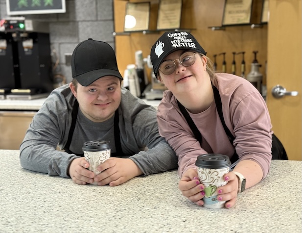 two students smiling and working at a coffee shop