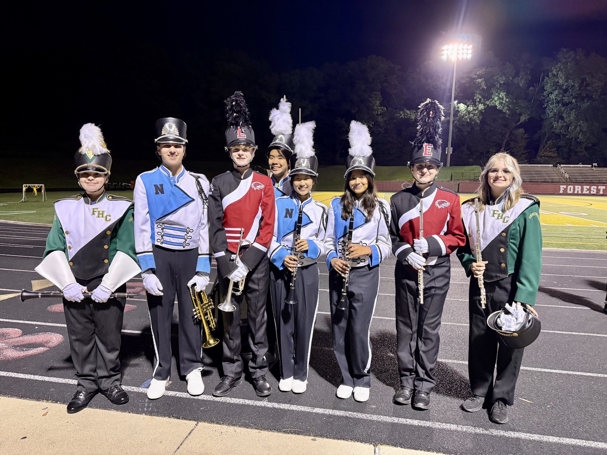 band members from each of the 3 forest hills schools posing for a picture on a track