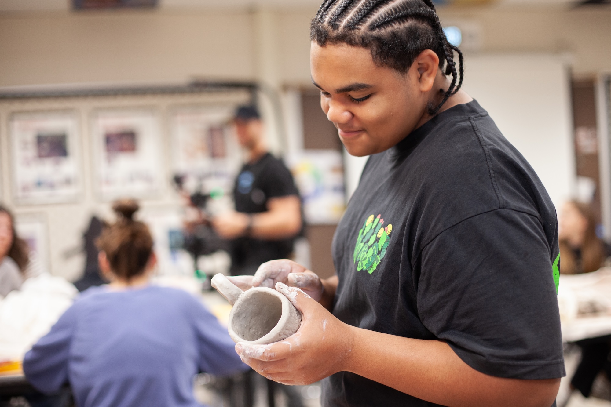 male student working on a clay mug in pottery class