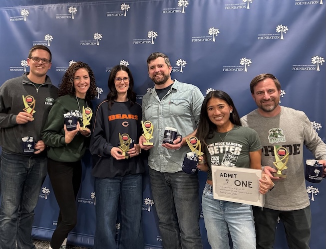 different people posing with trophies and unique mugs in front of a background screen