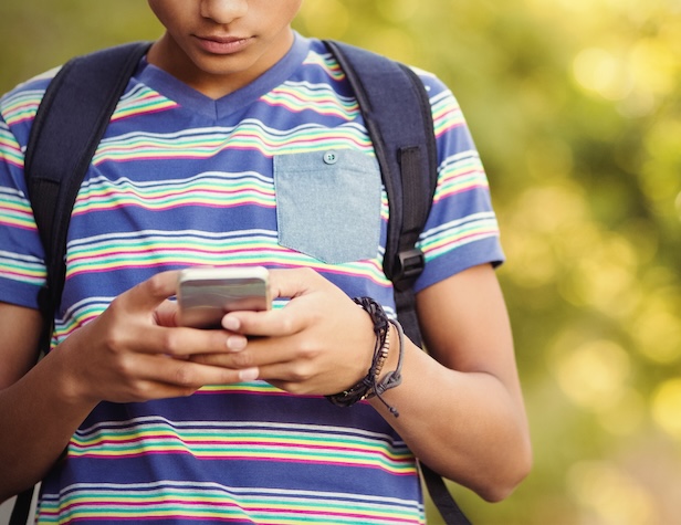 student walking with backpack on while looking down at his phone