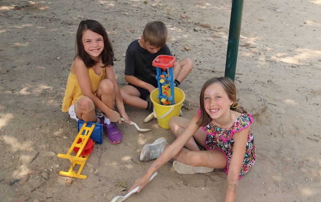 young students playing outside on the sand with toys