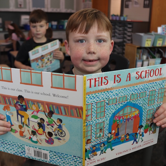 Student holding a book up, smiling