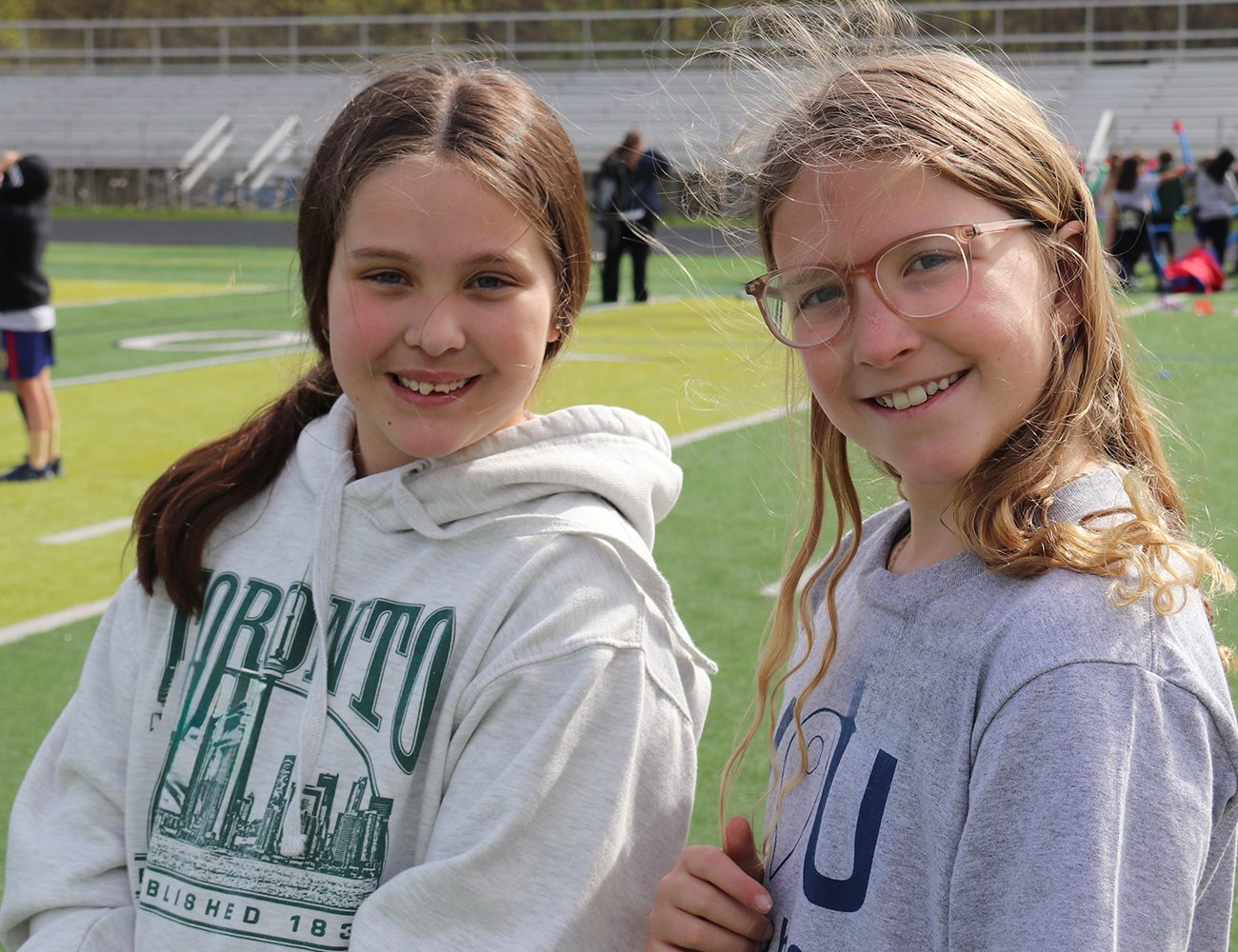 two middle school age girls in sweatshirts stand on a football field